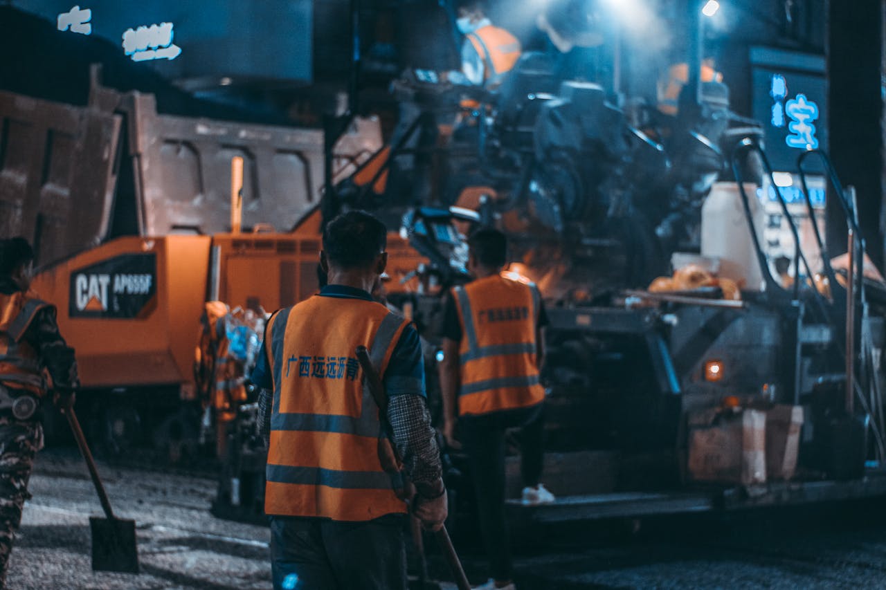 gallery-02 Workers in safety vests operate heavy machinery at a night construction site.