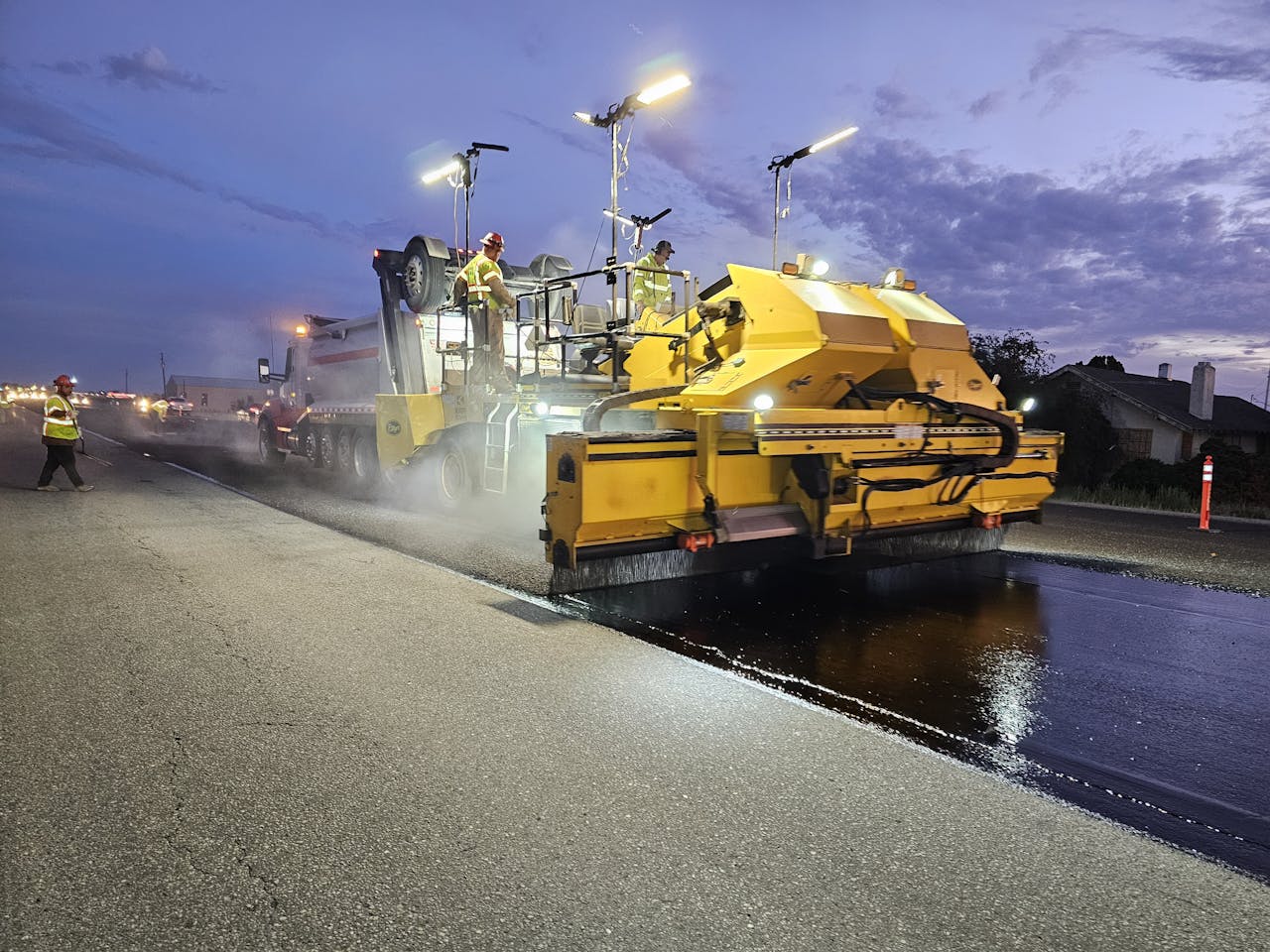 services-02 Workers operate heavy machinery to pave a road at twilight, enhancing infrastructure.