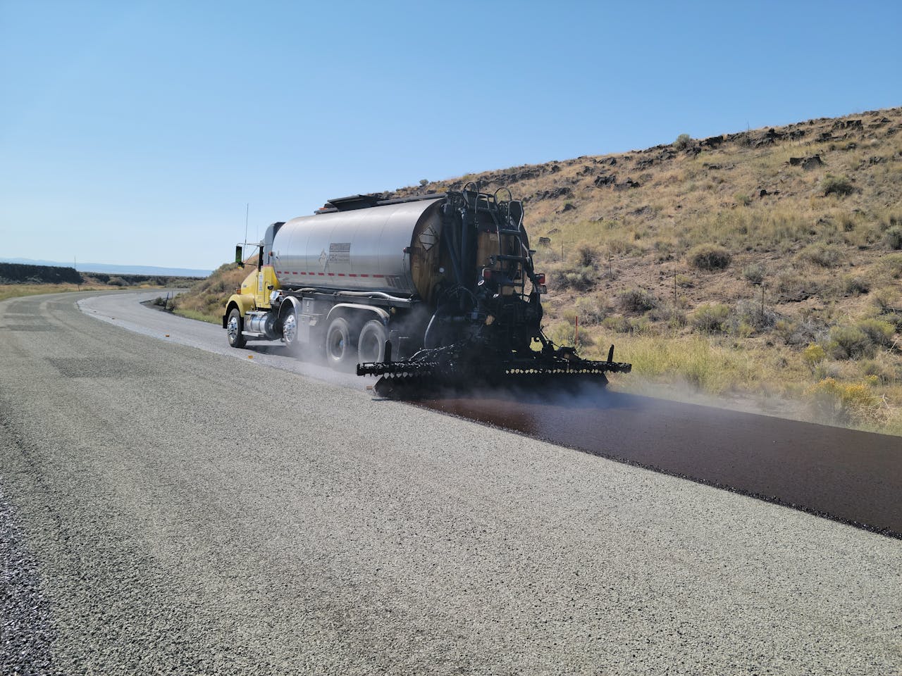 cta-02 A road tanker applying asphalt on a rural road in Oregon under clear skies.